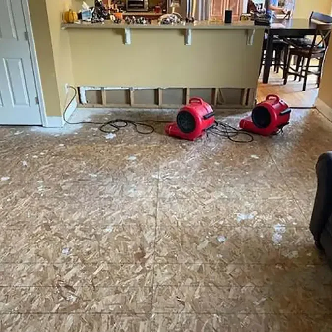 Red air movers stand on exposed subfloor beside a kitchen counter