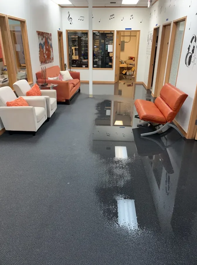 Standing water reflects overhead lights across a lobby with chairs and opened lower walls