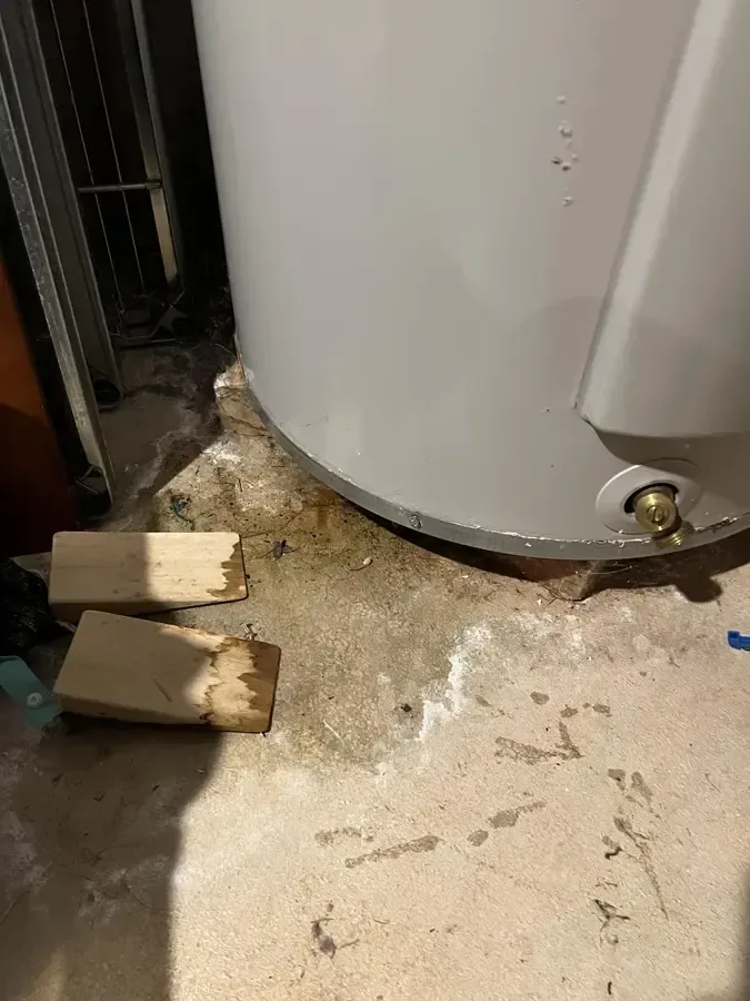 Water surrounds the base of a tank water heater beside loose wooden blocks